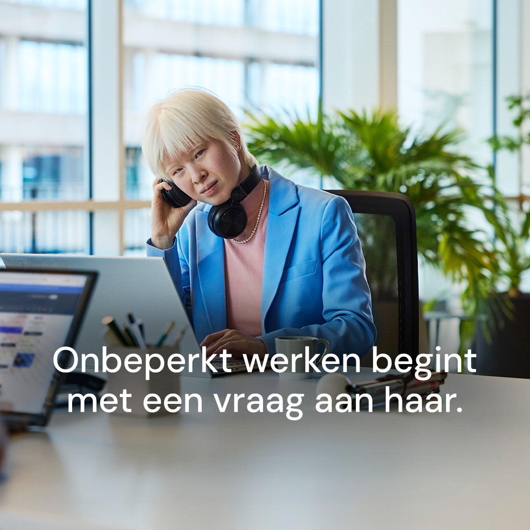 Campagnebeeld voor een carrousel: “Onbeperkt werken begint met een vraag aan haar.” Een vrouw zit achter een laptop op kantoor en houdt een koptelefoon tegen haar oor.